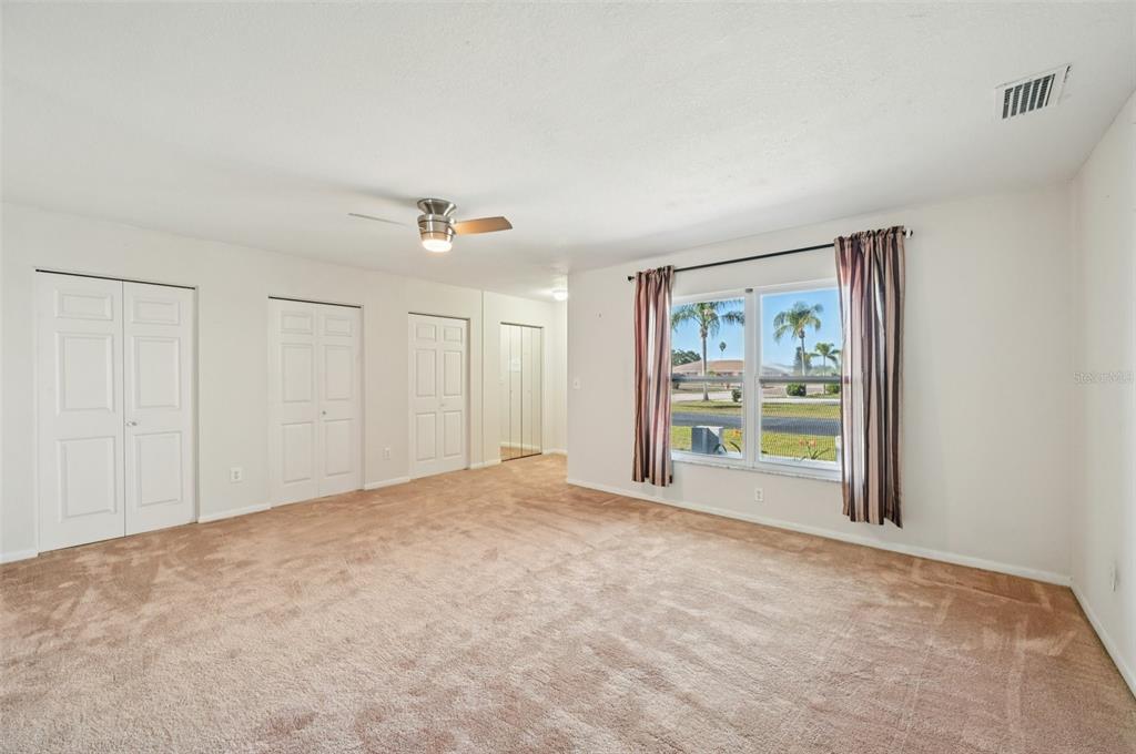 A carpeted bedroom features white walls, multiple closet doors, and a window with curtains — 332 CLUB MANOR DRIVE, SUN CITY CENTER, FL