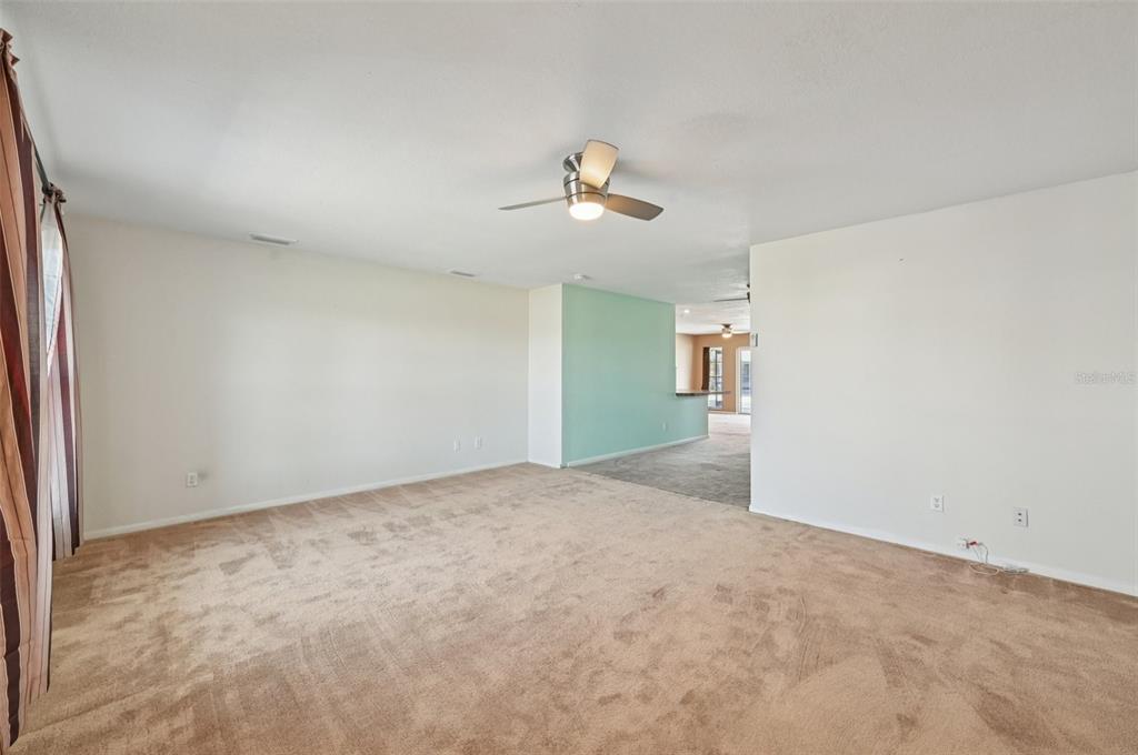 A carpeted living room features a ceiling fan, white walls, and an accent wall — 332 CLUB MANOR DRIVE, SUN CITY CENTER, FL