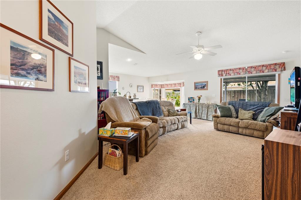 A living room features beige carpeting, a ceiling fan, and two brown fabric sofas — 6937 42ND COURT E, SARASOTA, FL
