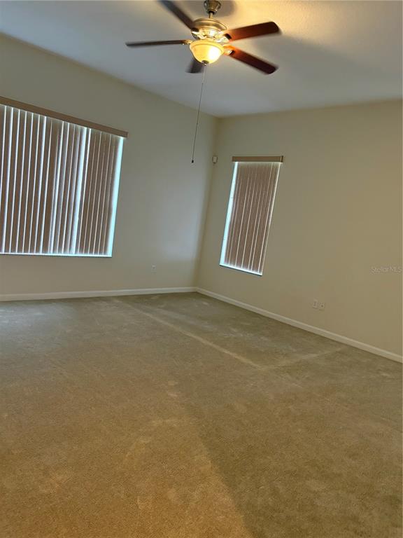 An empty room features beige carpet, light-colored walls, vertical blinds on two windows, and a ceiling fan — 3822 SHOREVIEW DRIVE, KISSIMMEE, FL