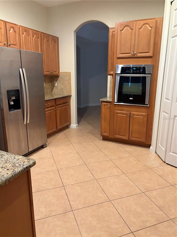 A kitchen features wood cabinets, stainless steel appliances, granite countertops, and light-colored tile flooring — 3822 SHOREVIEW DRIVE, KISSIMMEE, FL
