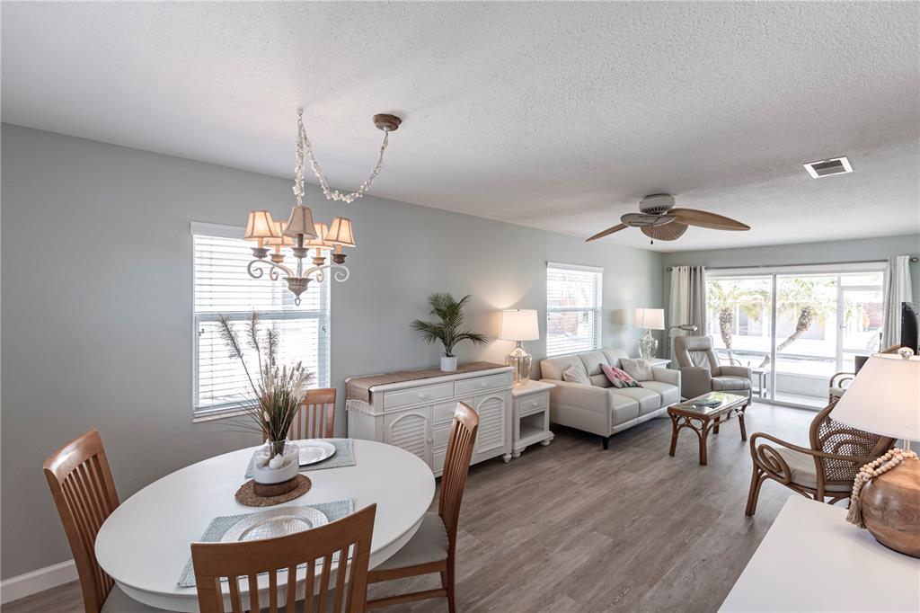 An open-concept living and dining area features light gray walls, wood-look flooring, and a chandelier — 6020 MIDNIGHT PASS ROAD UNIT 20, SARASOTA, FL
