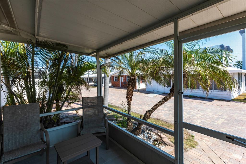 A screened-in porch with two chairs and a table overlooks a paved outdoor area — 6020 MIDNIGHT PASS ROAD UNIT 20, SARASOTA, FL