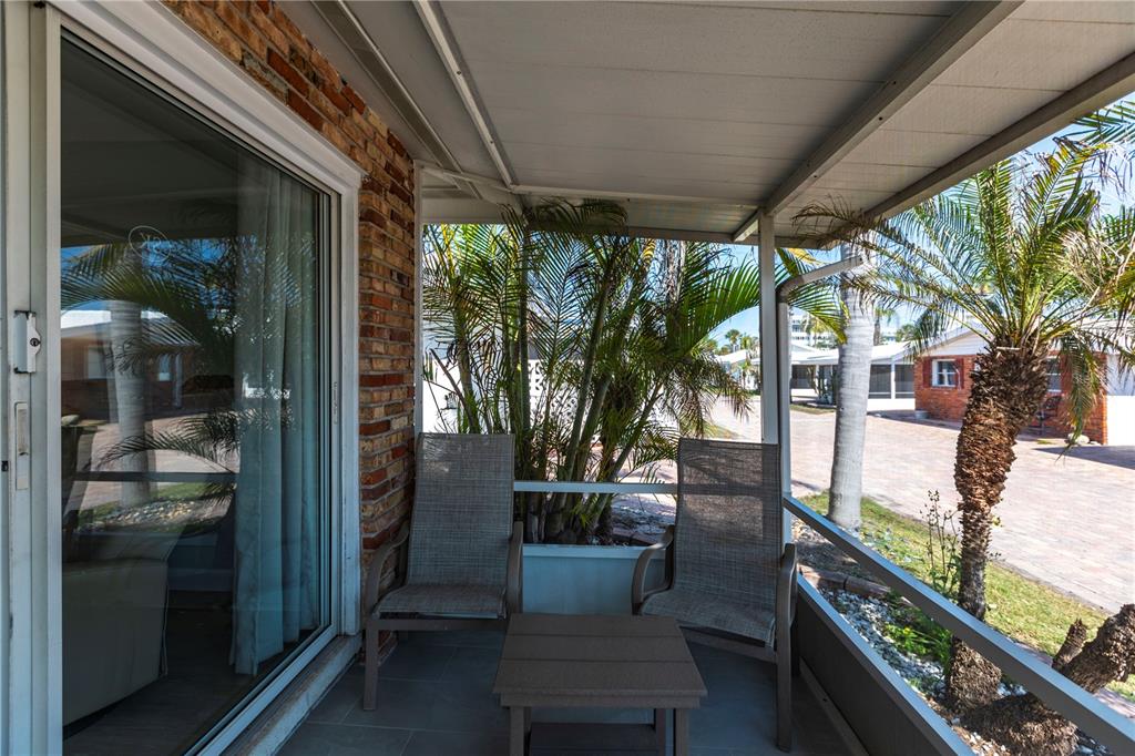 A covered patio features two chairs, a small table, brick siding, and a screen enclosure — 6020 MIDNIGHT PASS ROAD UNIT 20, SARASOTA, FL