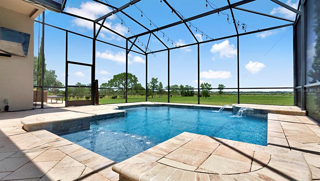 A screened-in patio features a swimming pool with water features and stone tile decking — 4911 PARKVIEW DRIVE, ST CLOUD, FL