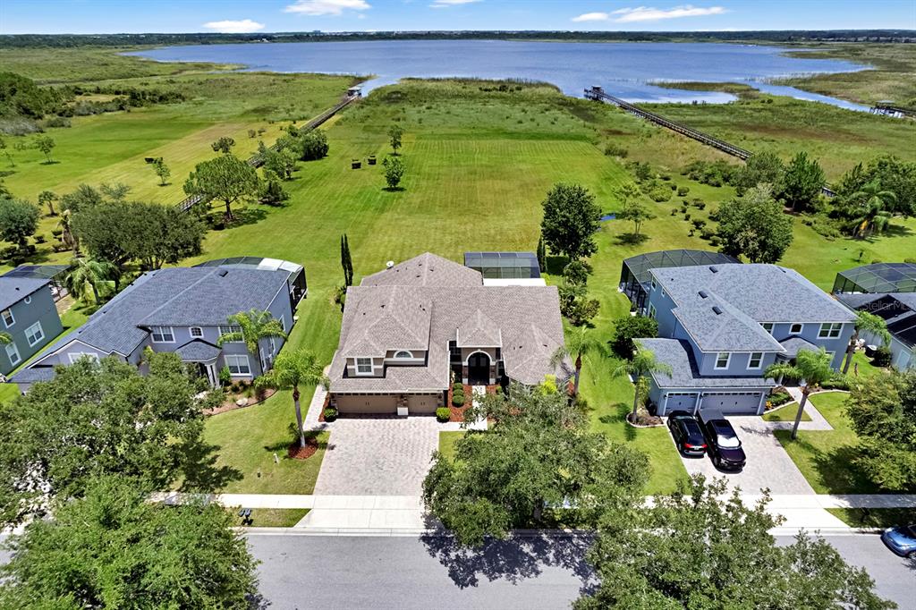 An aerial view shows three suburban houses with pools situated on a large grassy waterfront lot — 4911 PARKVIEW DRIVE, ST CLOUD, FL
