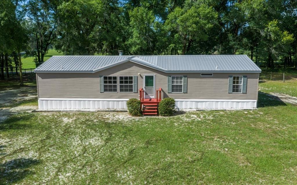 A single-story manufactured home with tan siding, a metal roof, and red front steps — 3551 NE 120TH STREET, ANTHONY, FL