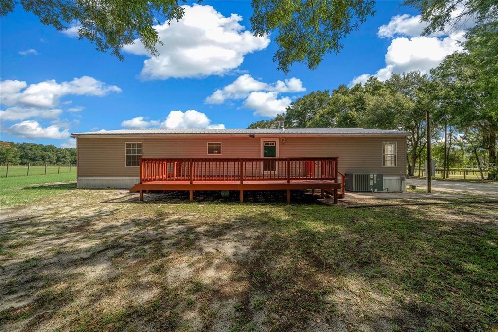 A single-story manufactured home with a large red wooden deck in a grassy yard — 3551 NE 120TH STREET, ANTHONY, FL