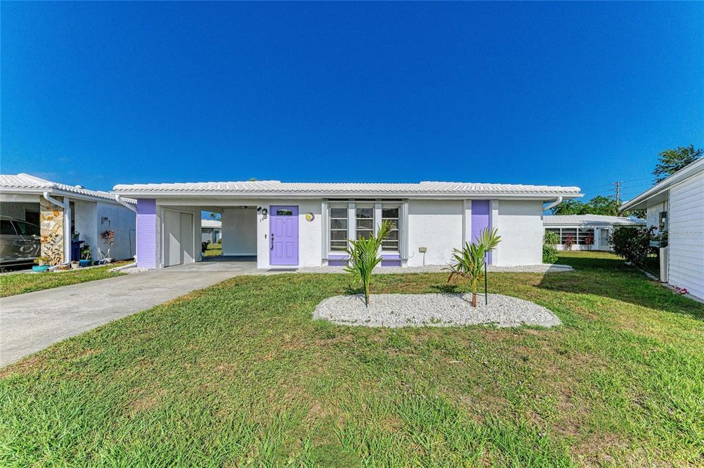 A single-story white house with a purple door and a carport under a clear sky — 140 CIRCLEWOOD DRIVE UNIT C1-4, VENICE, FL