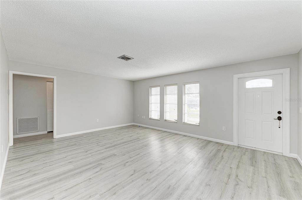 An empty living room with light gray walls, wood-look flooring, and a white front door — 140 CIRCLEWOOD DRIVE UNIT C1-4, VENICE, FL