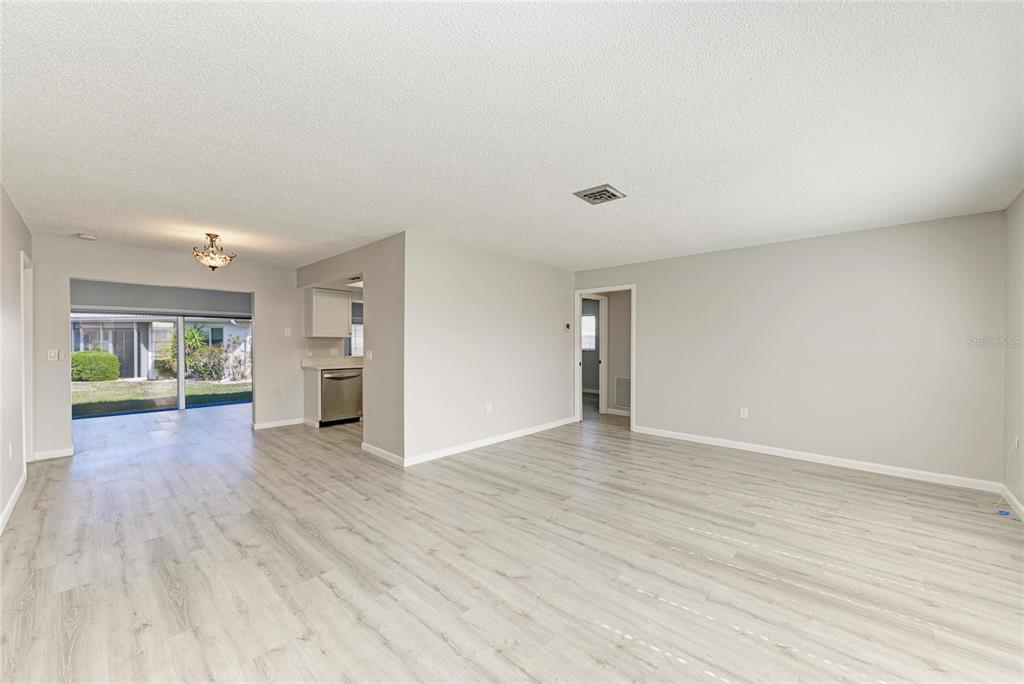 An open-concept living area features light wood-look flooring, neutral walls, and a sliding glass door — 140 CIRCLEWOOD DRIVE UNIT C1-4, VENICE, FL