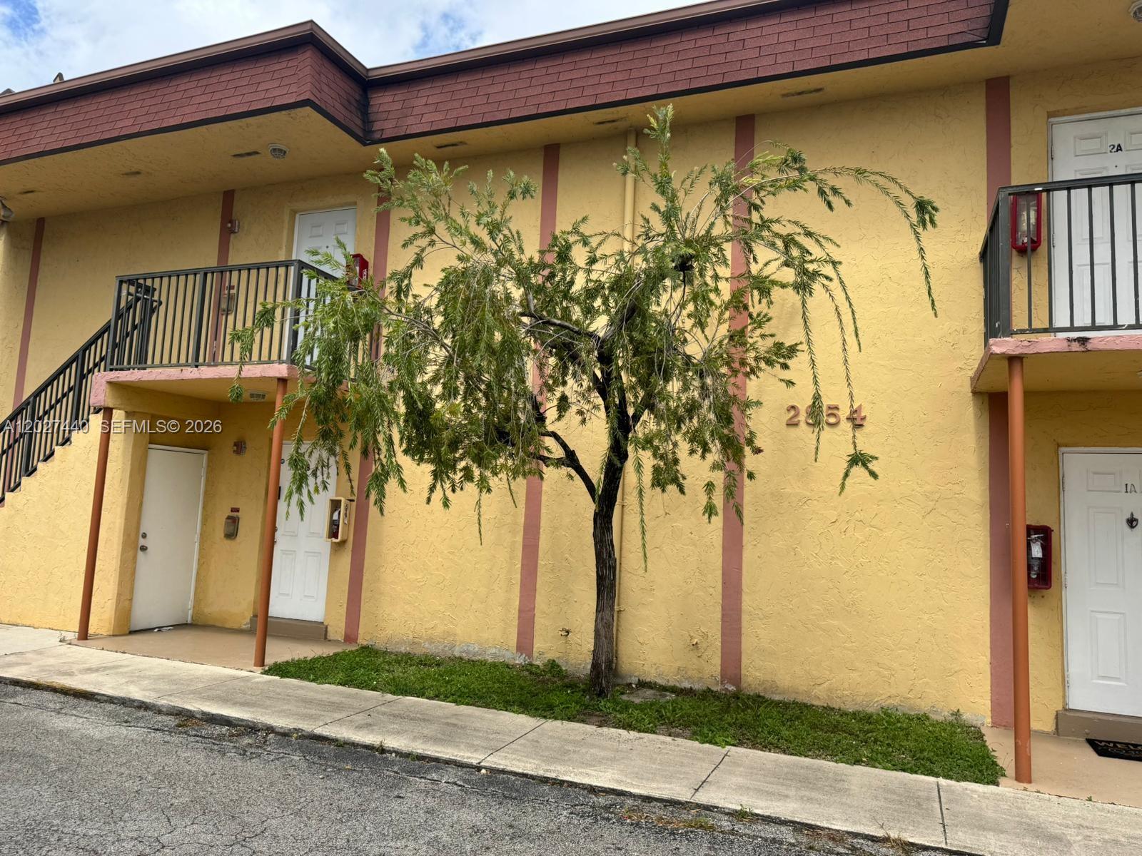 A yellow two-story apartment building exterior features a small weeping tree in front — 2854 NW 55th Ave # 2B, Lauderhill FL 33313, LAUDERHILL, FL