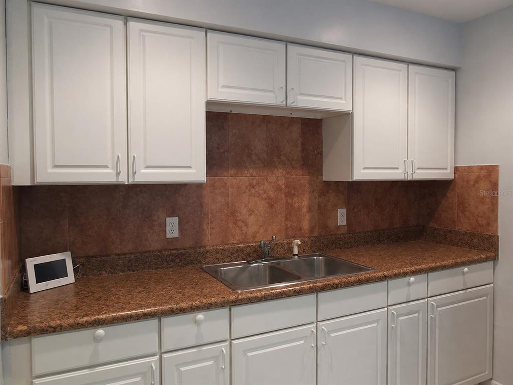 A kitchen features white cabinets, a black refrigerator, a black stove, and tan tile flooring — 1427 PLEASANT PLACE, LAKELAND, FL