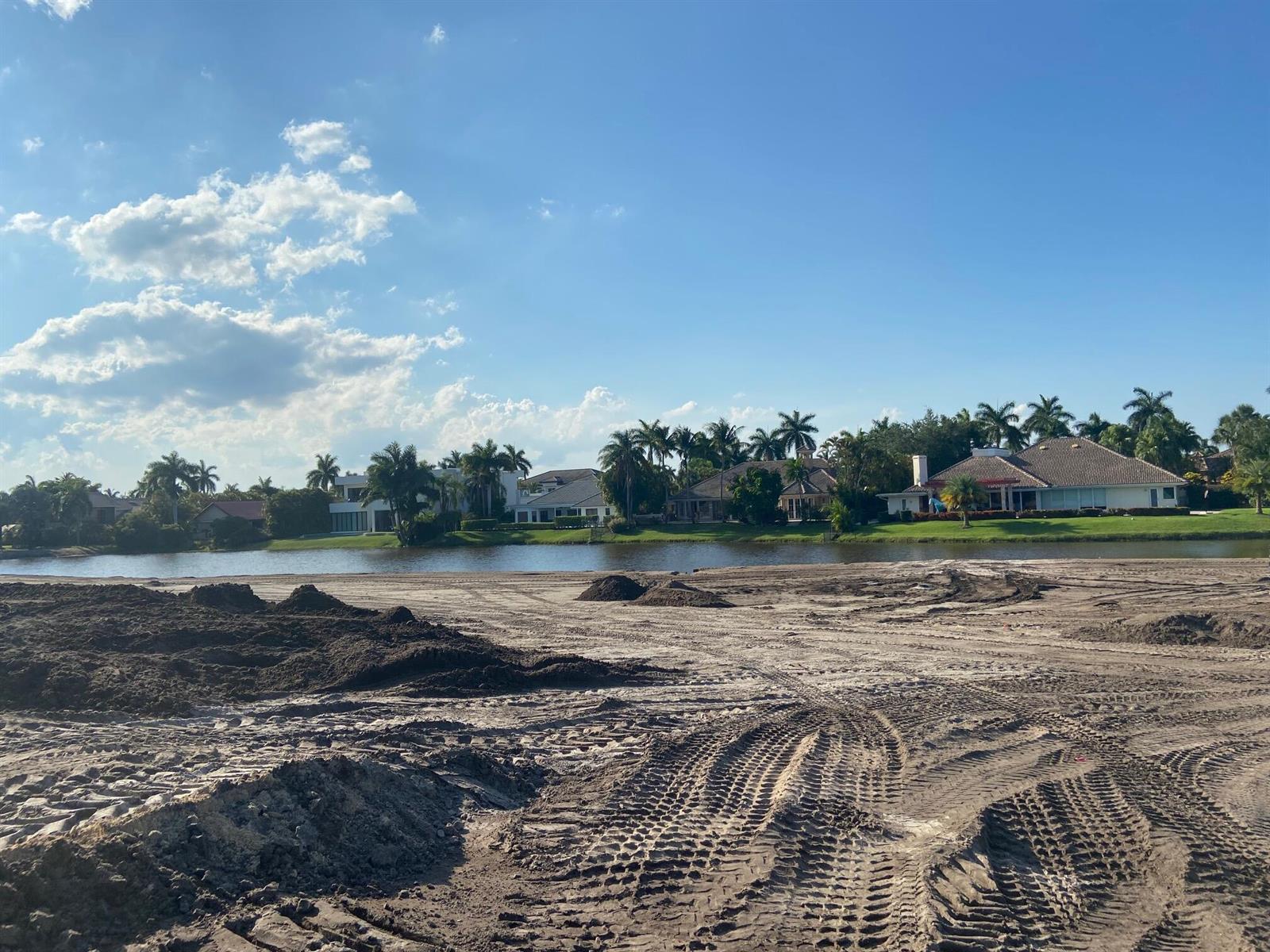 A construction site with tire tracks in the dirt overlooks a lake and residential houses — 4100 Clint Moore Road, Boca Raton FL 33496, BOCA RATON, FL