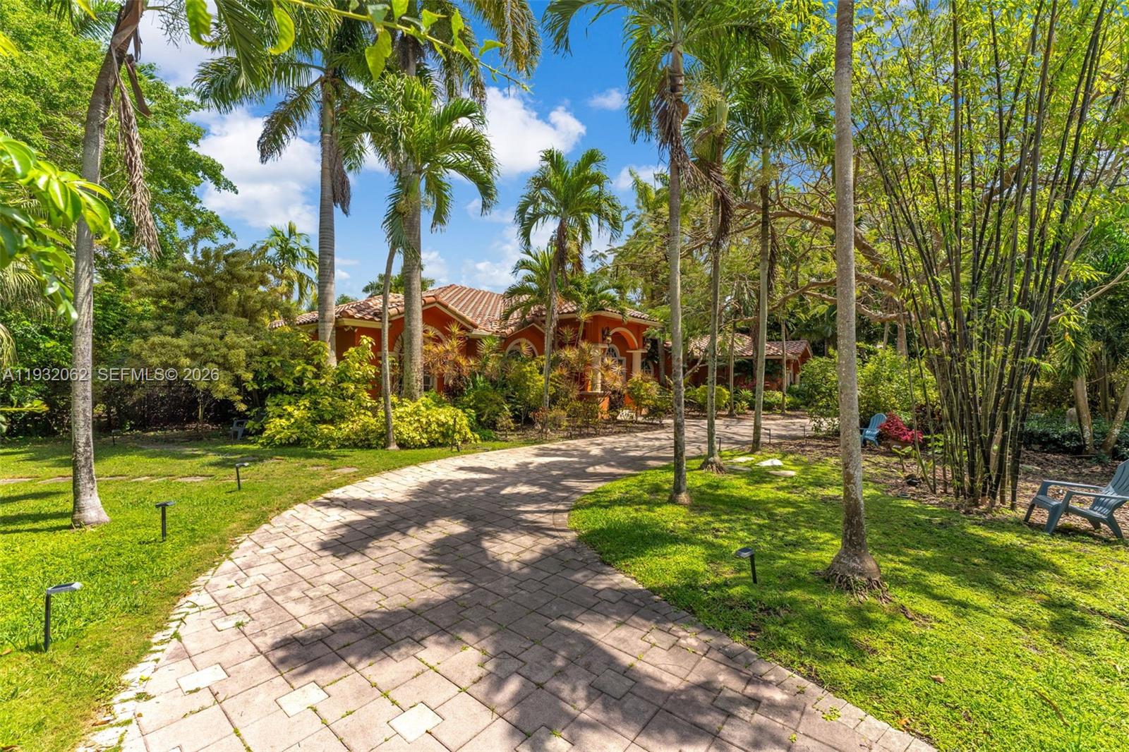 A paved driveway leads to a terracotta-roofed house surrounded by lush tropical landscaping and palms — 11825 S Mitchell Manor Cir, Pinecrest FL 33156, PINECREST, FL