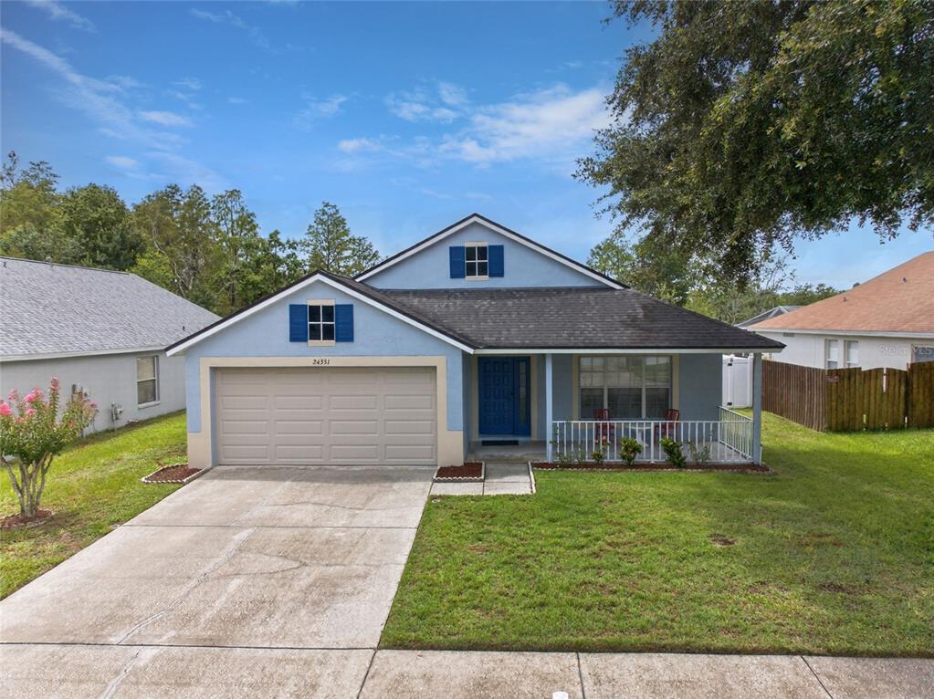A light blue single-story house features a two-car garage, a front porch, and blue shutters — 24331 CROSSCUT ROAD, LUTZ, FL