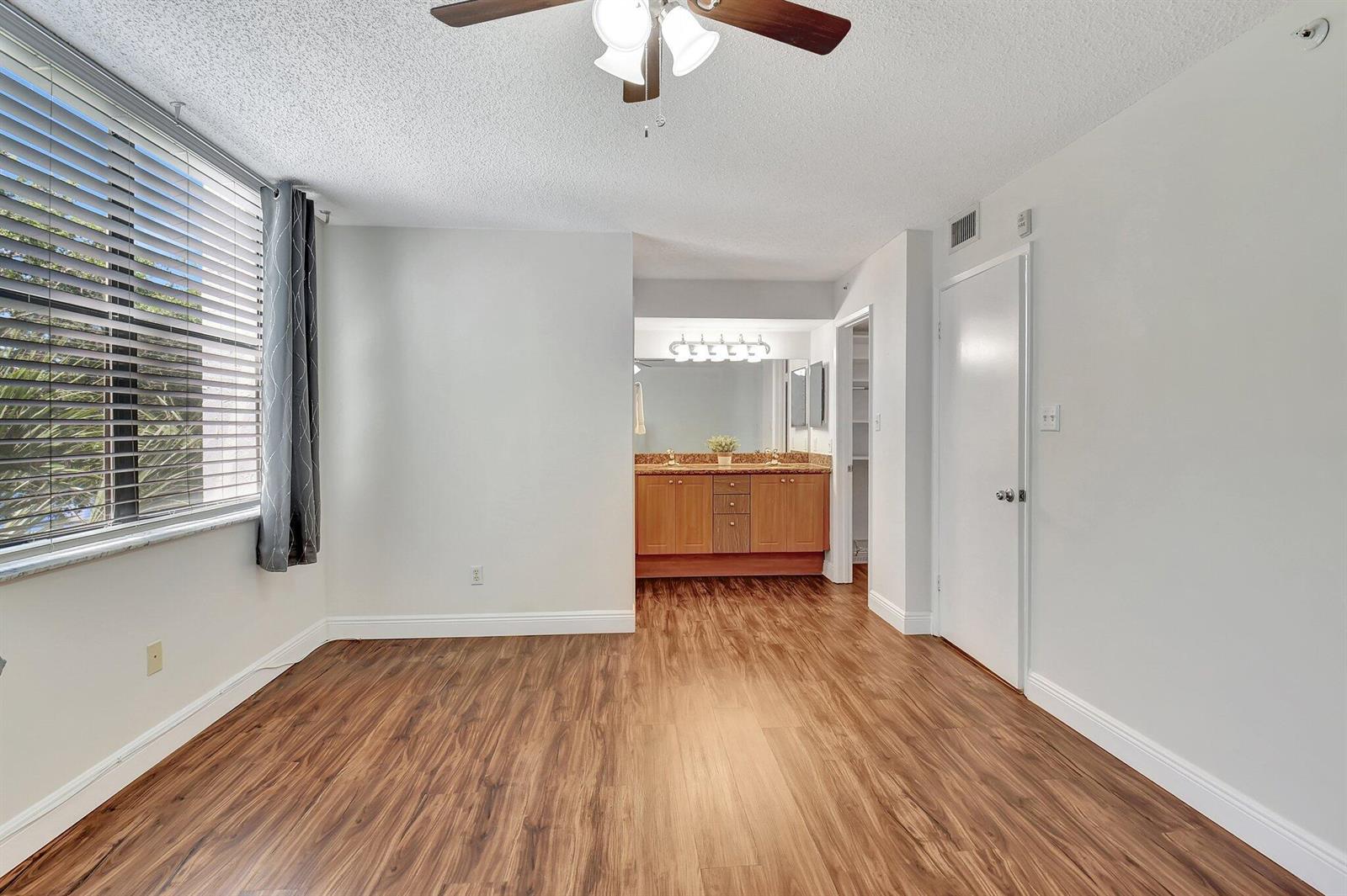 A bedroom with wood-look flooring, a ceiling fan, and an open vanity area — 820 Lavers Circle # G402, Delray Beach FL 33444, DELRAY BEACH, FL