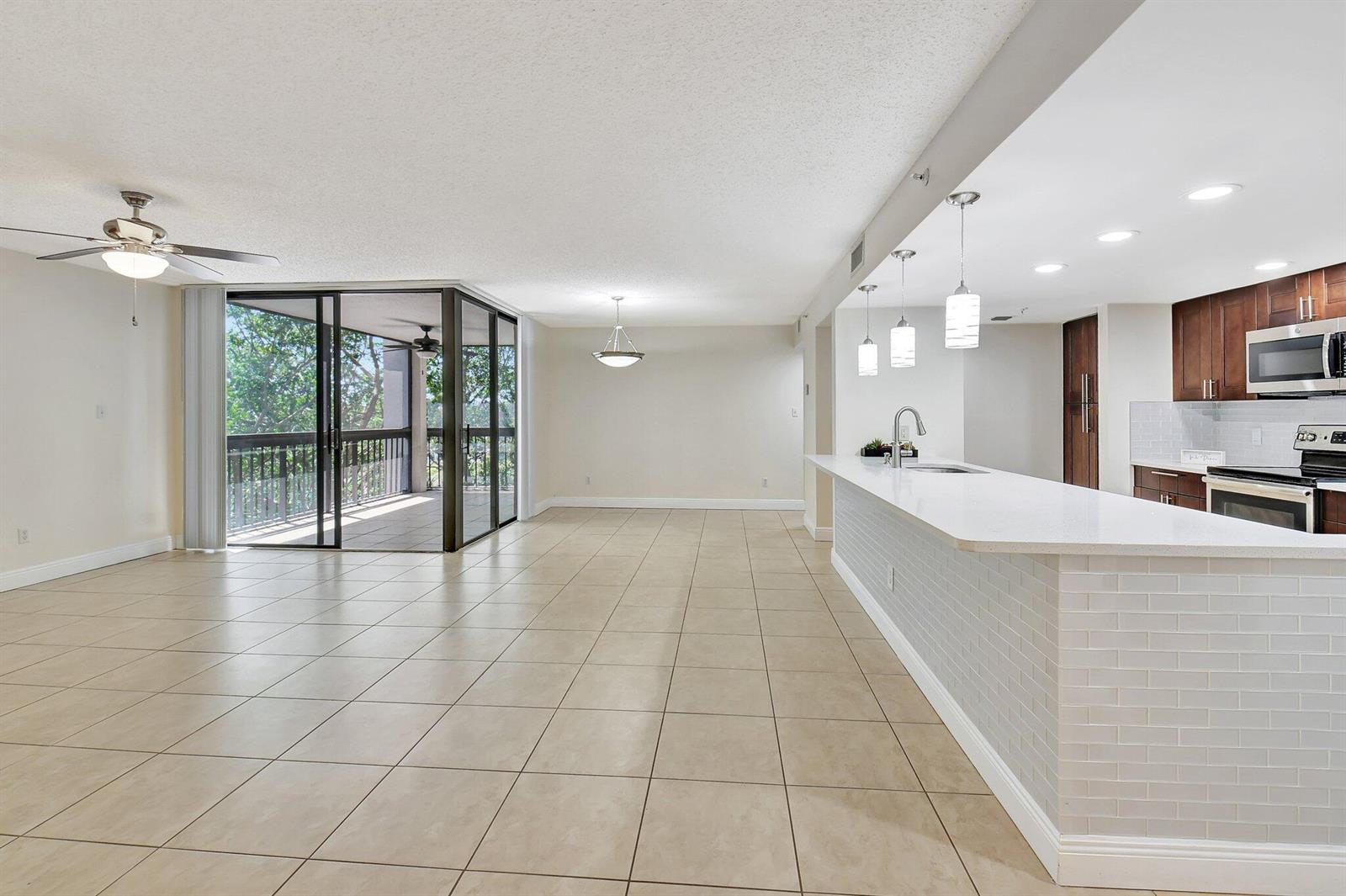 An open-concept living and dining area features tile flooring, a kitchen island, and a balcony — 820 Lavers Circle # G402, Delray Beach FL 33444, DELRAY BEACH, FL