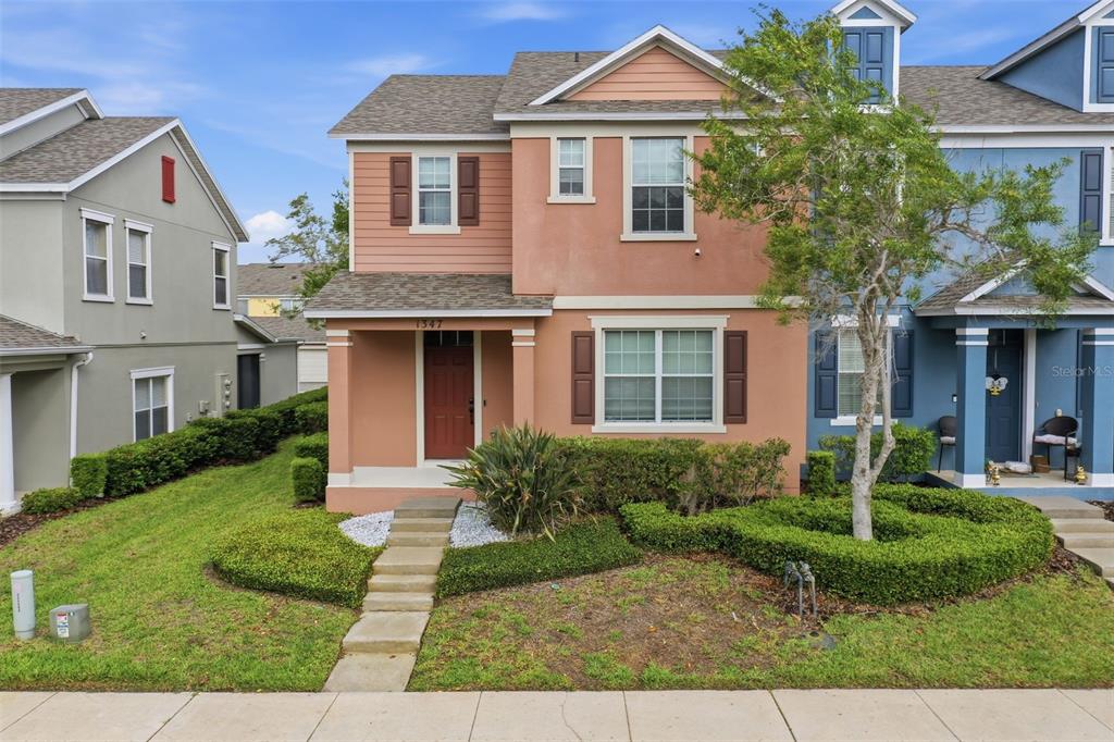 A two-story house with a peach-colored stucco facade, a brown front door, and manicured landscaping — 1347 ALSTON BAY BOULEVARD, APOPKA, FL