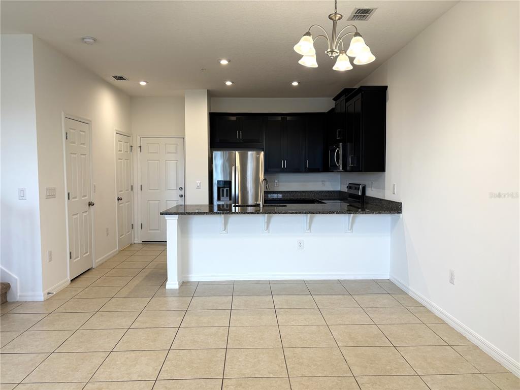 A kitchen with dark cabinets, granite countertops, and tile flooring features a breakfast bar — 10009 EAGLE ROCK ALLEY, ORLANDO, FL