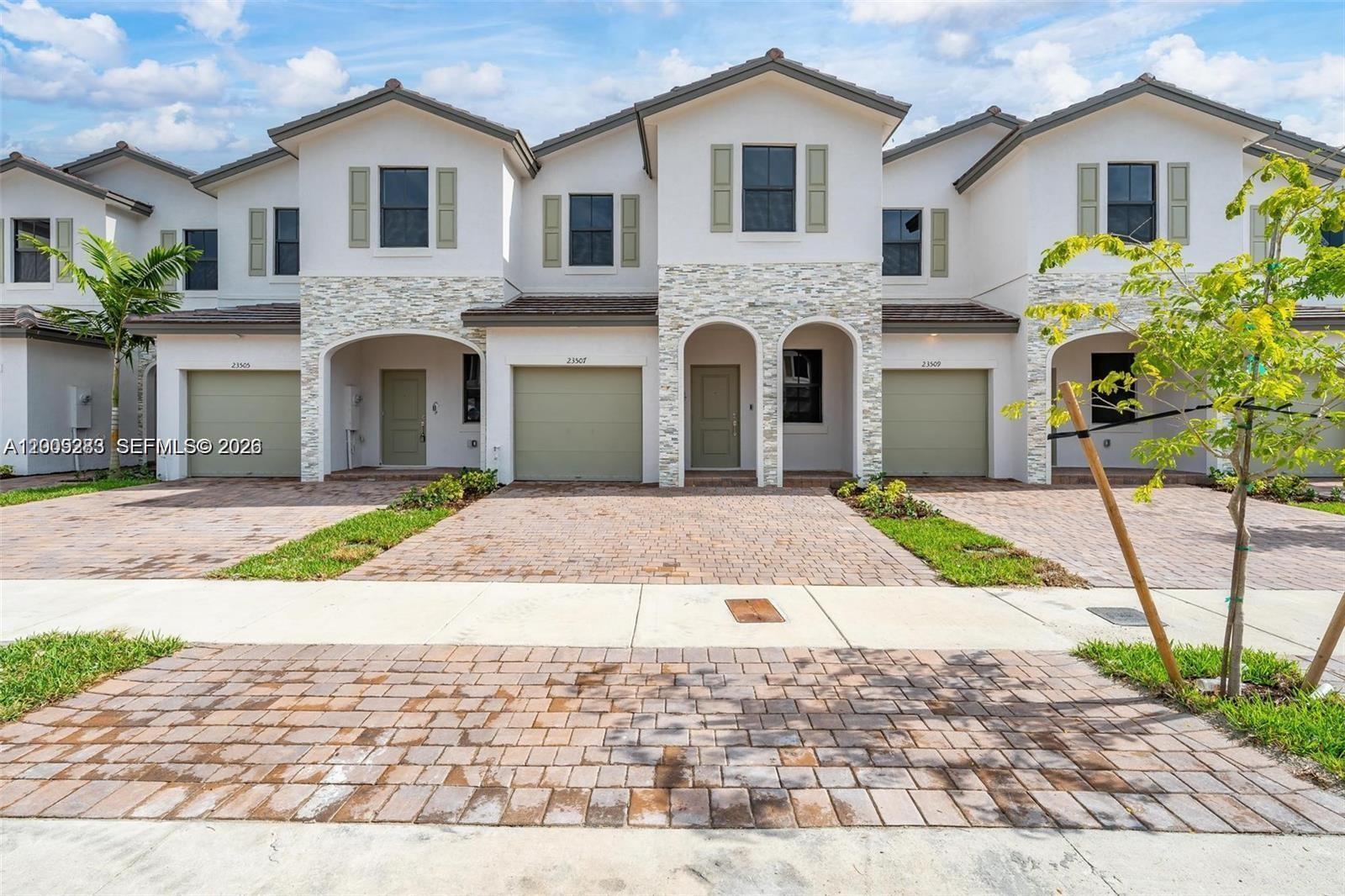 A row of three modern townhouses features white stucco, stone accents, and paved driveways — 23507 SW 129th Path, Homestead FL 33032, HOMESTEAD, FL