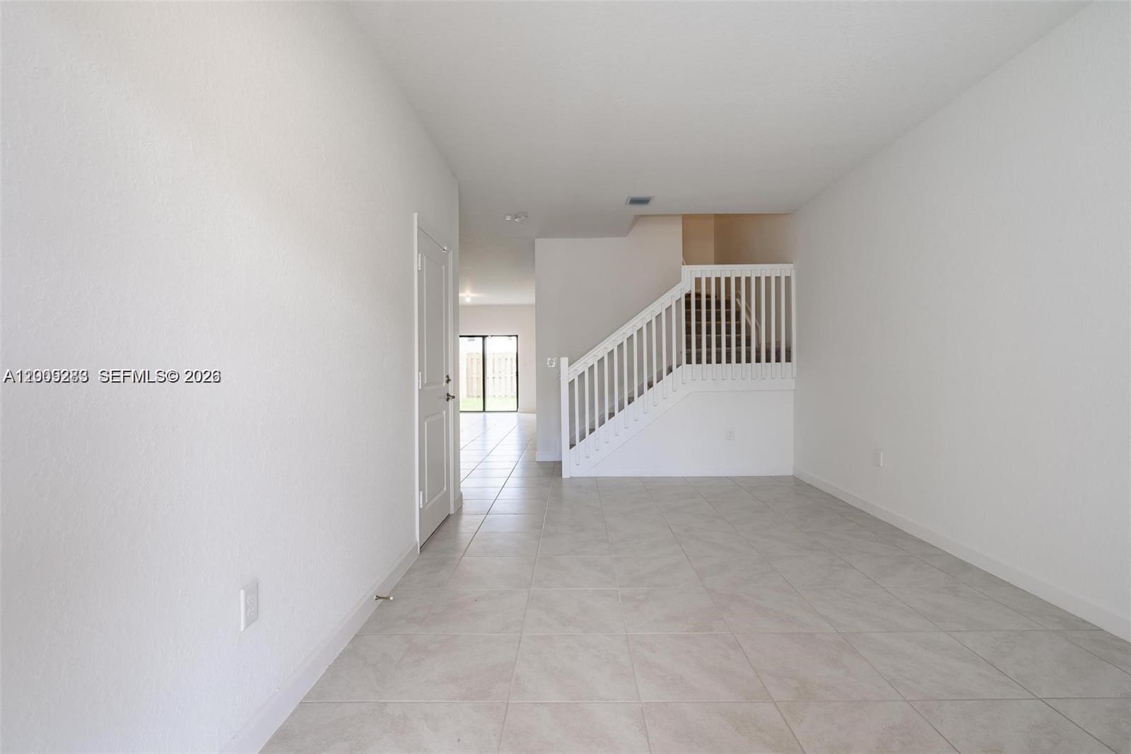 An empty room features white walls, tile flooring, and a staircase with a white railing — 23507 SW 129th Path, Homestead FL 33032, HOMESTEAD, FL