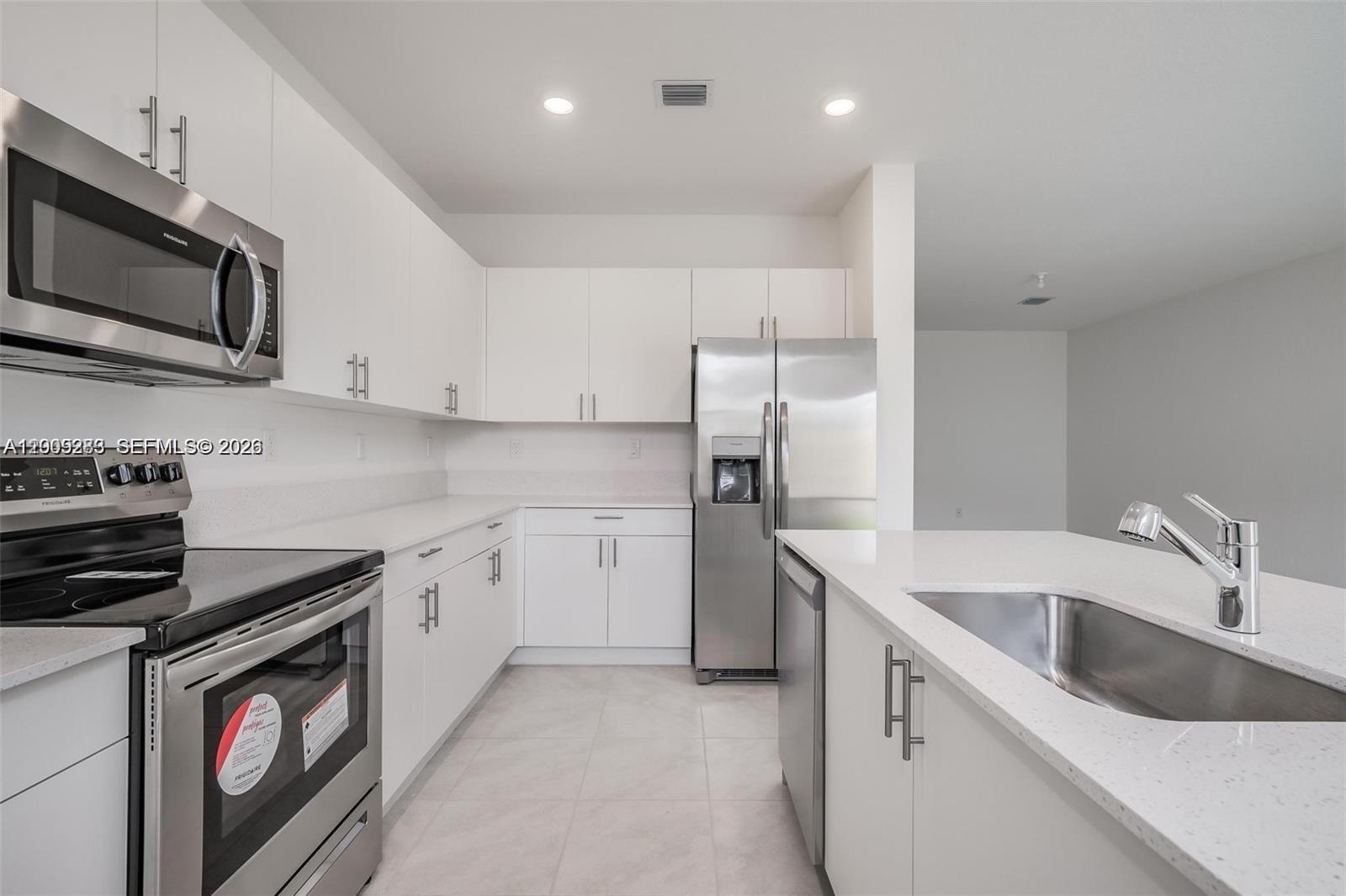A modern kitchen features white cabinetry, stainless steel appliances, and a quartz-topped island — 23507 SW 129th Path, Homestead FL 33032, HOMESTEAD, FL