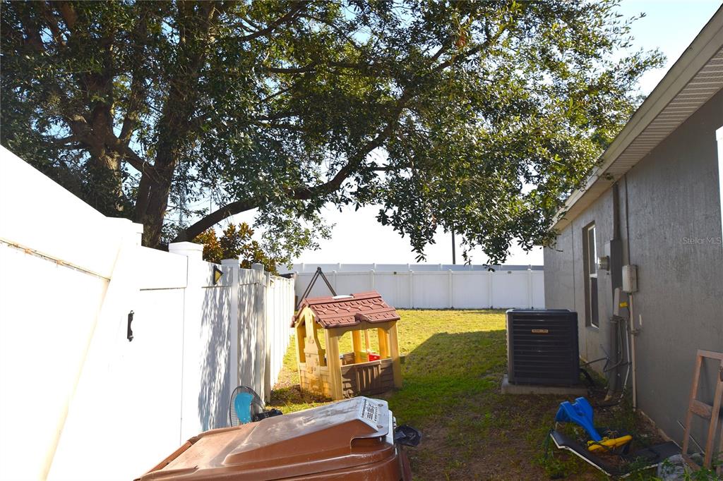 A backyard features a white vinyl fence, a playhouse, an air conditioning unit, and trees — 500 LAKE CHARLES DRIVE, DAVENPORT, FL