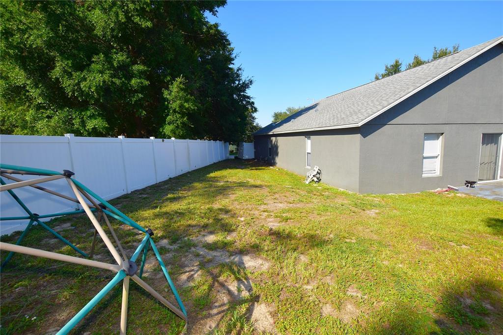 A backyard features a white vinyl fence, a gray house, and a metal climbing dome — 500 LAKE CHARLES DRIVE, DAVENPORT, FL