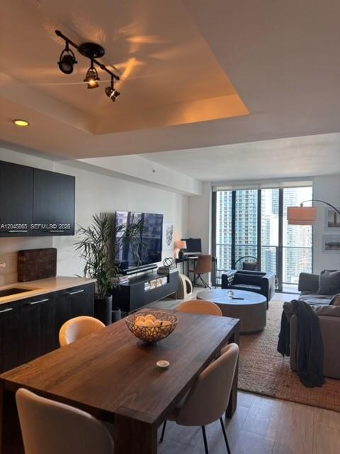 A modern open-concept living and dining area features dark cabinetry, a wooden table, and floor-to-ceiling windows — 55 SW 9th St # 3104, Miami FL 33130, MIAMI, FL