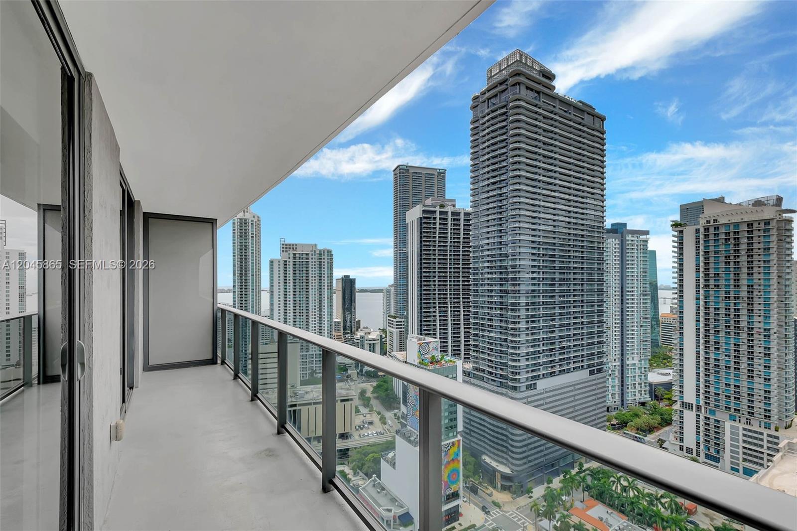 A high-rise balcony overlooks a dense city skyline with multiple skyscrapers and a distant bay — 55 SW 9th St # 3104, Miami FL 33130, MIAMI, FL
