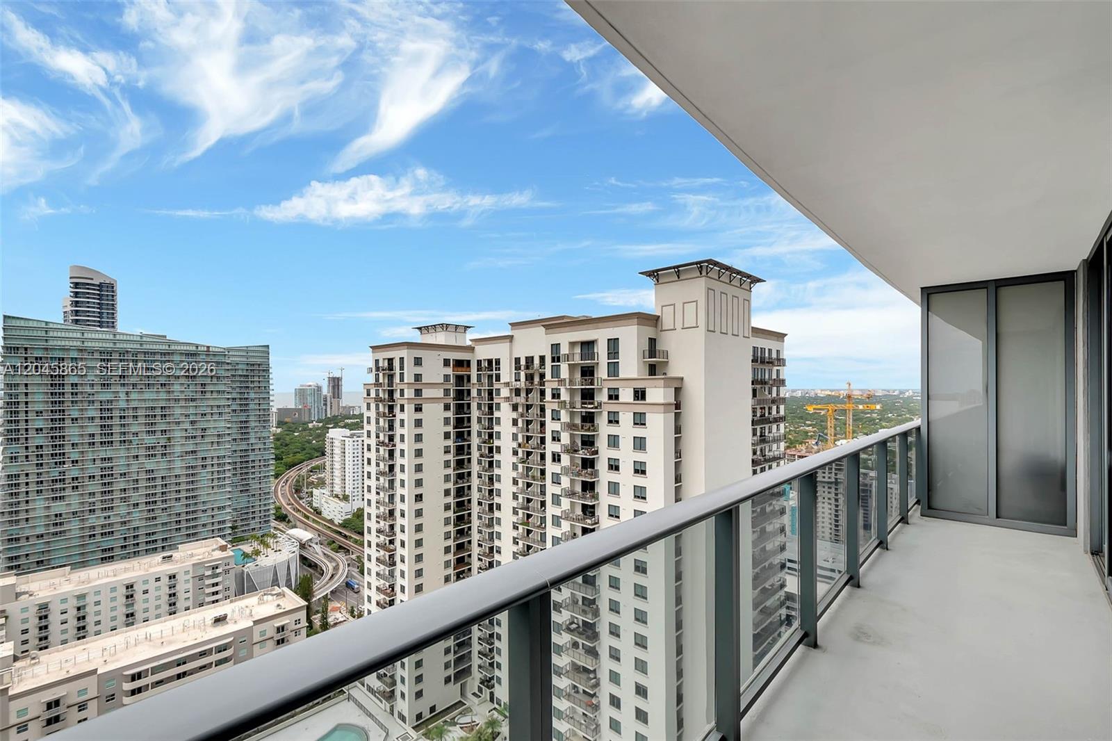 A high-rise balcony with a glass railing overlooks a city skyline and nearby buildings — 55 SW 9th St # 3104, Miami FL 33130, MIAMI, FL