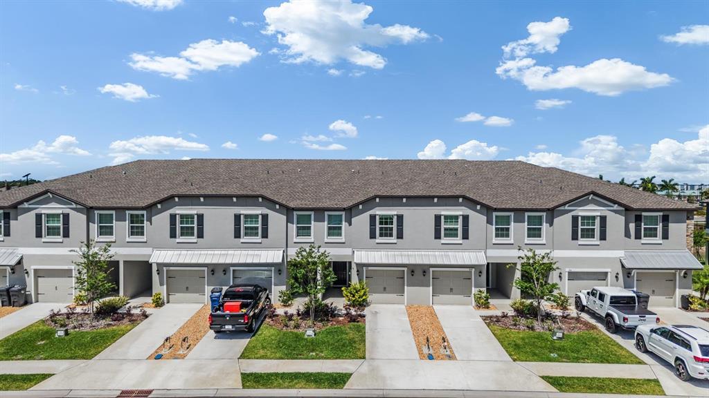 An exterior view of a multi-unit townhouse building with gray siding and attached garages — 9133 BONITA MAR DRIVE, PARRISH, FL