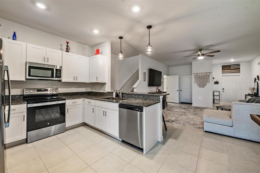 A kitchen with white cabinets, stainless steel appliances, and granite countertops opens to a living area — 9133 BONITA MAR DRIVE, PARRISH, FL