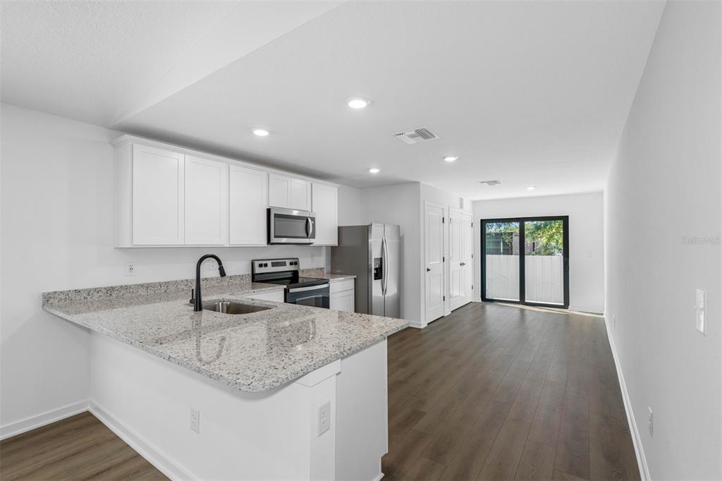 A kitchen with white cabinets, granite countertops, and stainless steel appliances opens to a living area — 590 BLACKTHORN DRIVE, LAKELAND, FL