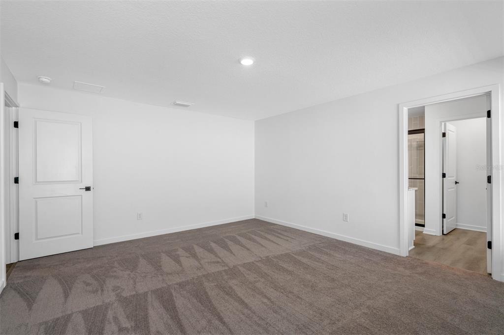 A carpeted bedroom with white walls, a closed door, and an open doorway to a bathroom — 590 BLACKTHORN DRIVE, LAKELAND, FL