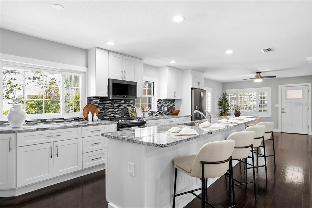 A modern kitchen features white cabinets, a granite island with four stools, and dark flooring — 2720 10TH STREET N, ST PETERSBURG, FL