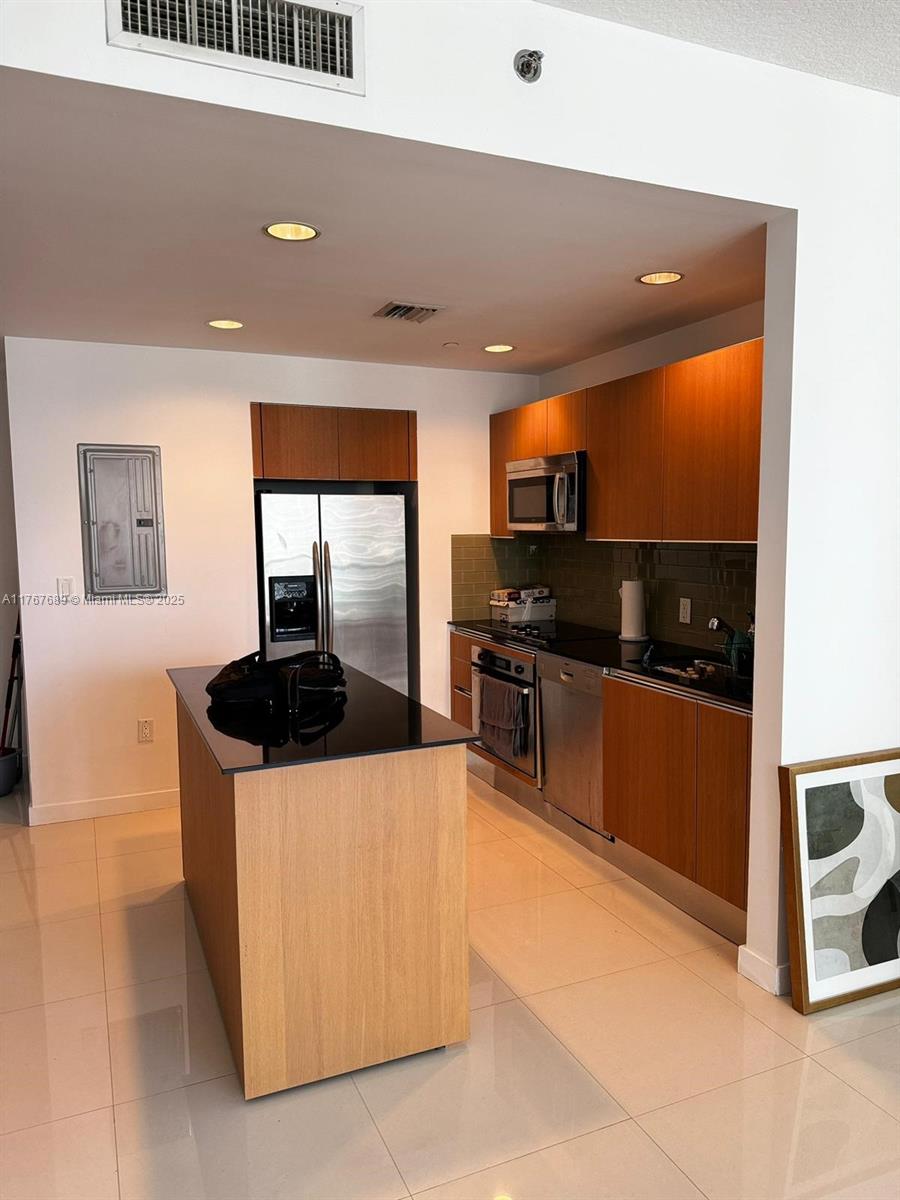 A modern kitchen features light wood cabinetry, a black island countertop, and stainless steel appliances — 1050 Brickell Ave # 2908, Miami FL 33131, MIAMI, FL