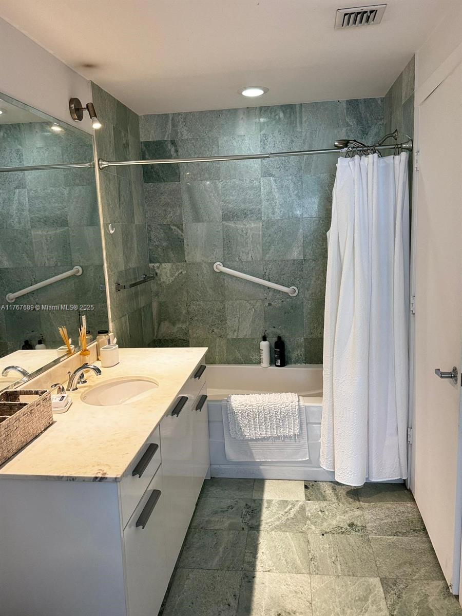 A bathroom features green stone tile walls, a white vanity, and a shower-tub combination — 1050 Brickell Ave # 2908, Miami FL 33131, MIAMI, FL