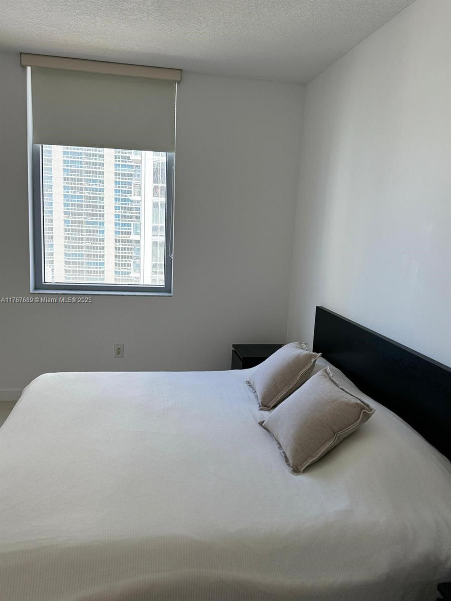 A bedroom features a white bed with two pillows, a black headboard, and a window — 1050 Brickell Ave # 2908, Miami FL 33131, MIAMI, FL