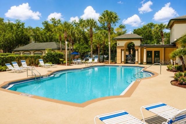A swimming pool is surrounded by lounge chairs and palm trees near a community building — 17102 CARRINGTON PARK DRIVE UNIT 302, TAMPA, FL