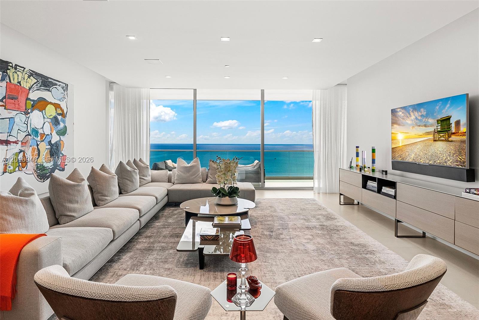 A modern living room features a large sectional sofa, glass coffee tables, and floor-to-ceiling ocean views — 10201 Collins Ave # 1806, Bal Harbour FL 33154, BAL HARBOUR, FL