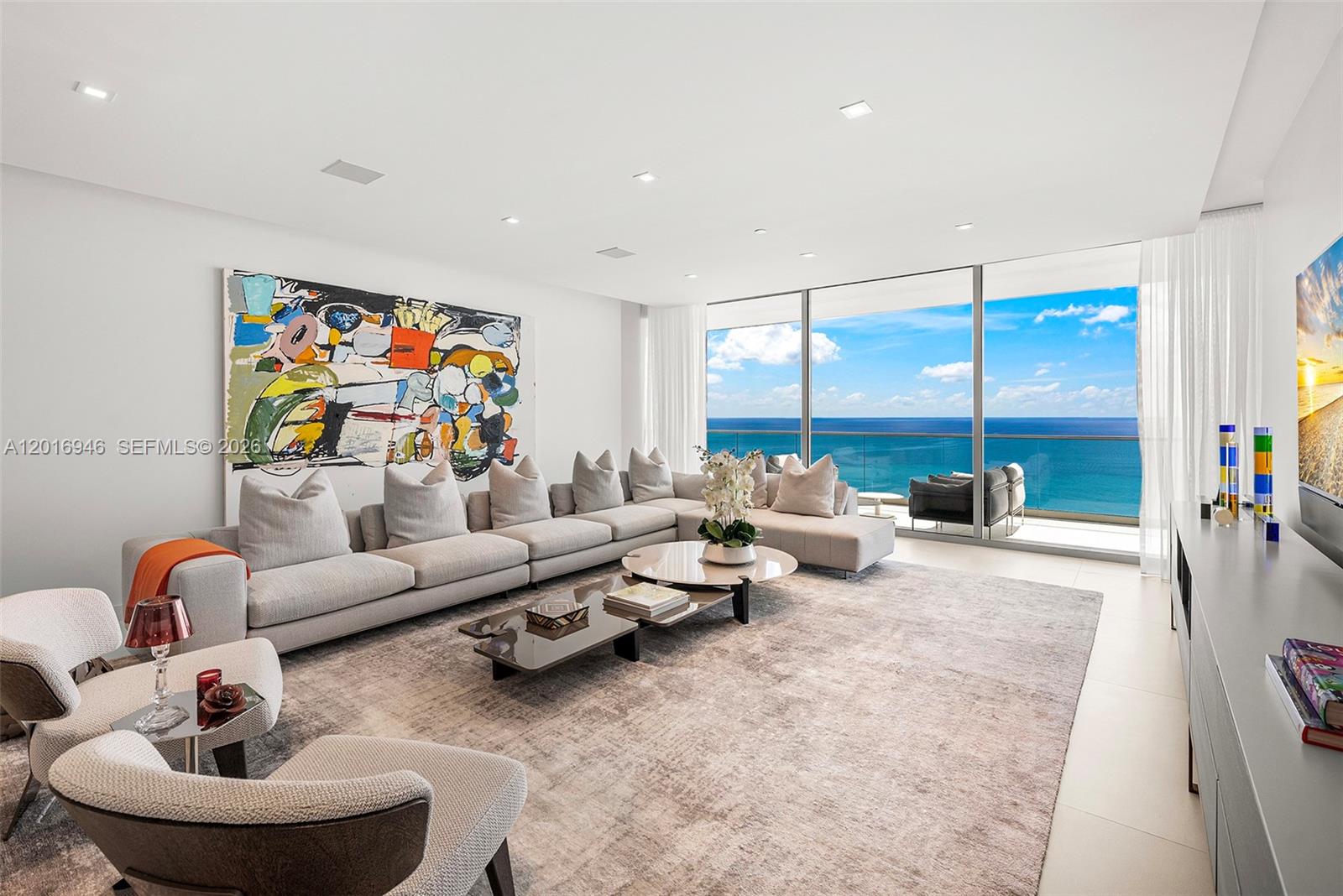 A modern living room features a large sectional sofa, abstract art, and floor-to-ceiling ocean views — 10201 Collins Ave # 1806, Bal Harbour FL 33154, BAL HARBOUR, FL