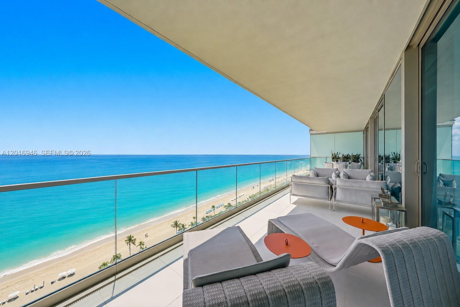 A spacious balcony features modern lounge furniture overlooking a sandy beach and the ocean — 10201 Collins Ave # 1806, Bal Harbour FL 33154, BAL HARBOUR, FL