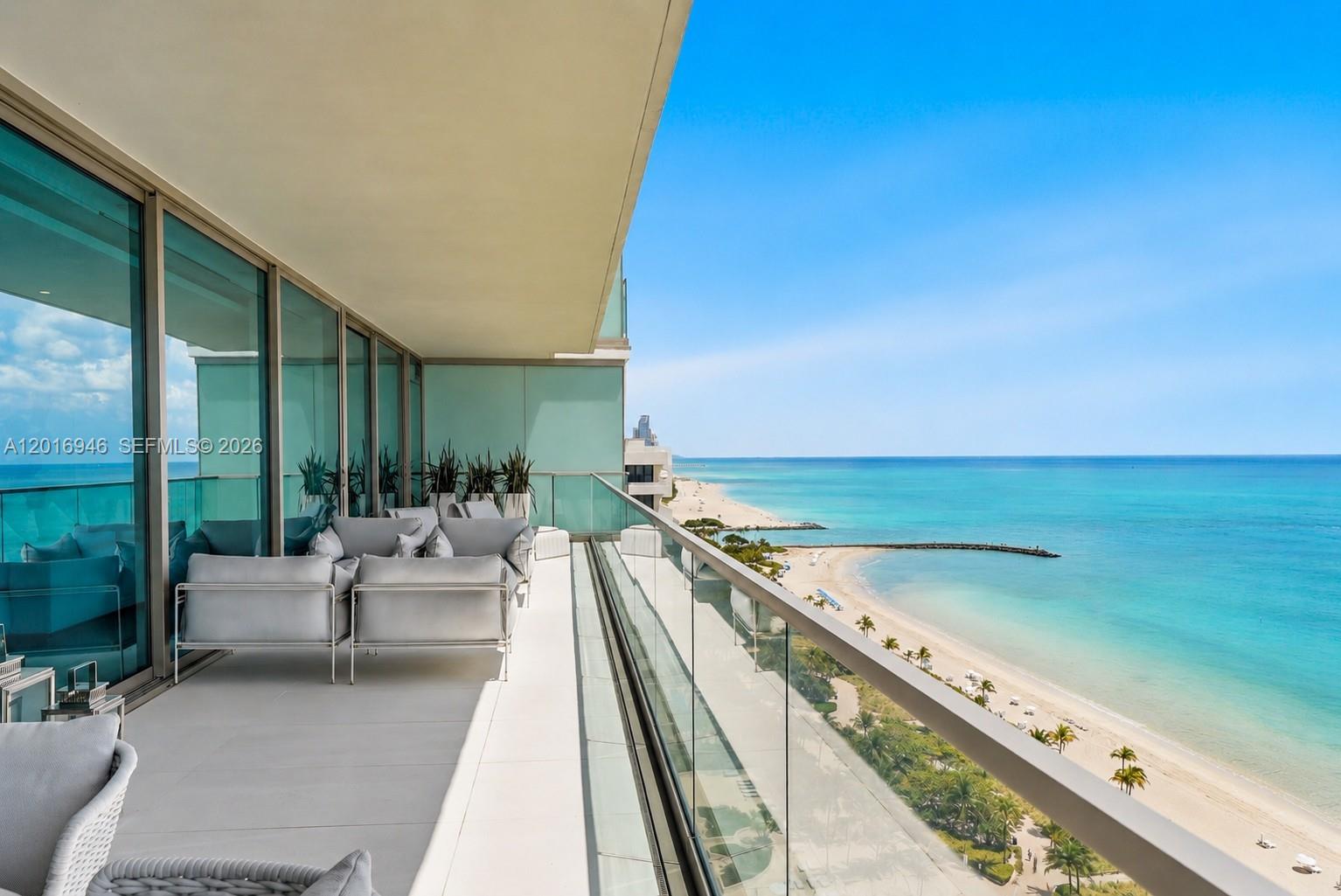 A balcony with modern outdoor seating overlooks a sandy beach and the ocean — 10201 Collins Ave # 1806, Bal Harbour FL 33154, BAL HARBOUR, FL