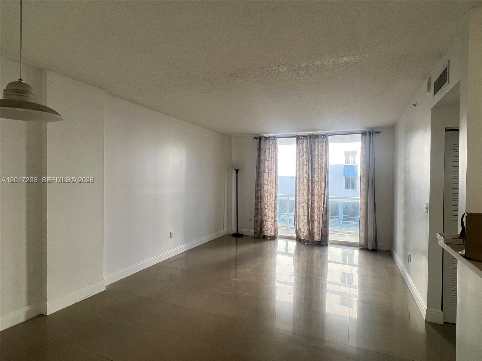 An empty living room features large beige floor tiles, white walls, and a glass balcony door — 5091 NW 7th St # 706, Miami FL 33126, MIAMI, FL