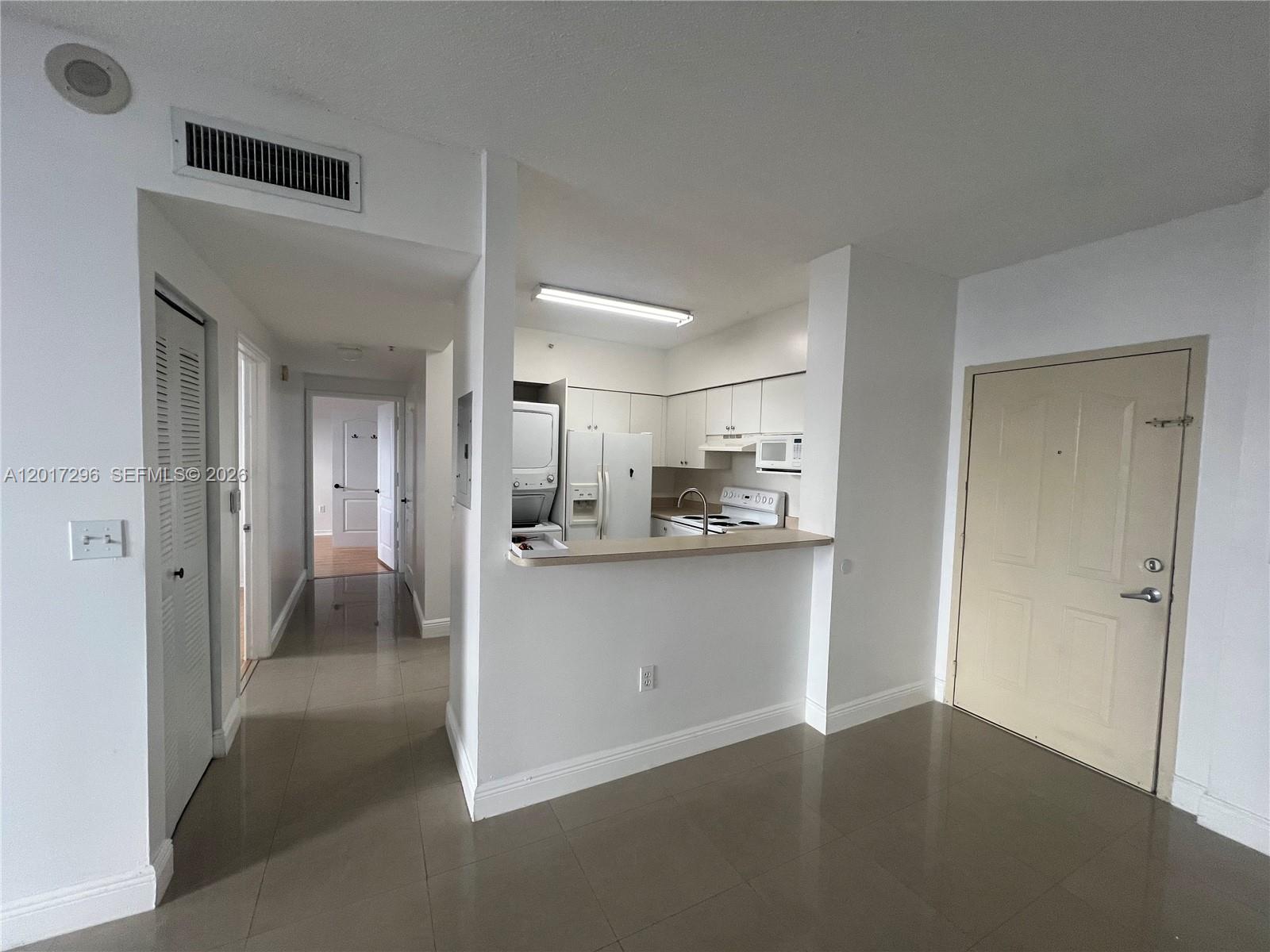 A kitchen with white cabinets and appliances overlooks a tiled living area and hallway — 5091 NW 7th St # 706, Miami FL 33126, MIAMI, FL