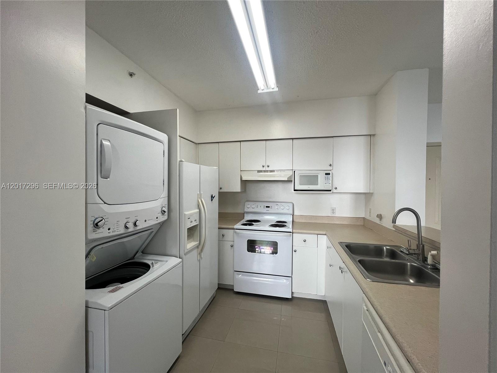 A white kitchen features a stacked washer and dryer, white appliances, and laminate countertops — 5091 NW 7th St # 706, Miami FL 33126, MIAMI, FL