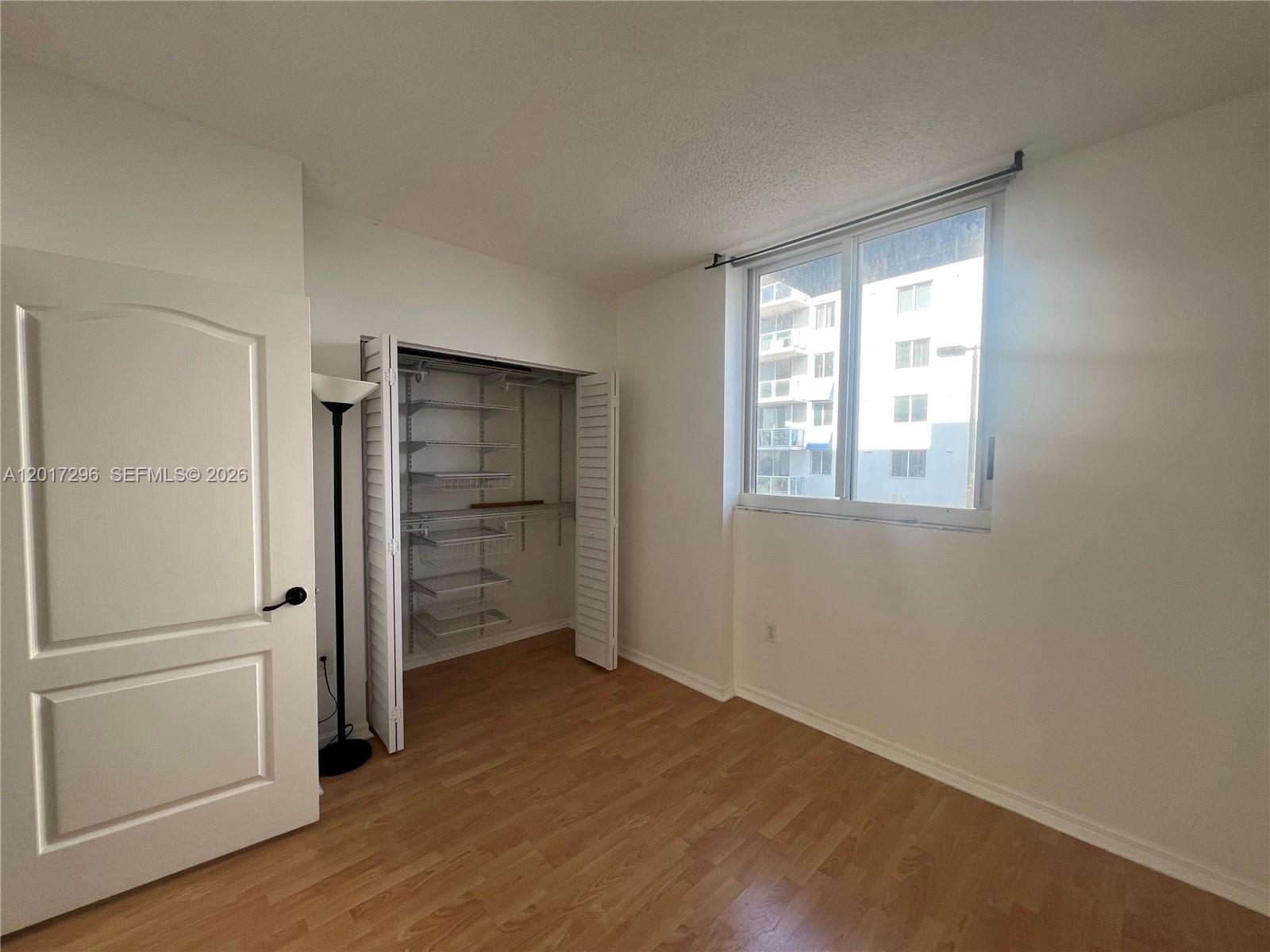 An empty bedroom features light wood-look flooring, a white closet with wire shelving, and a window — 5091 NW 7th St # 706, Miami FL 33126, MIAMI, FL