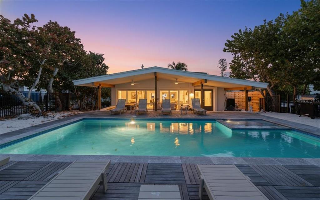 A swimming pool with a deck and lounge chairs sits before a modern single-story house — 102 TUNA STREET, ANNA MARIA, FL